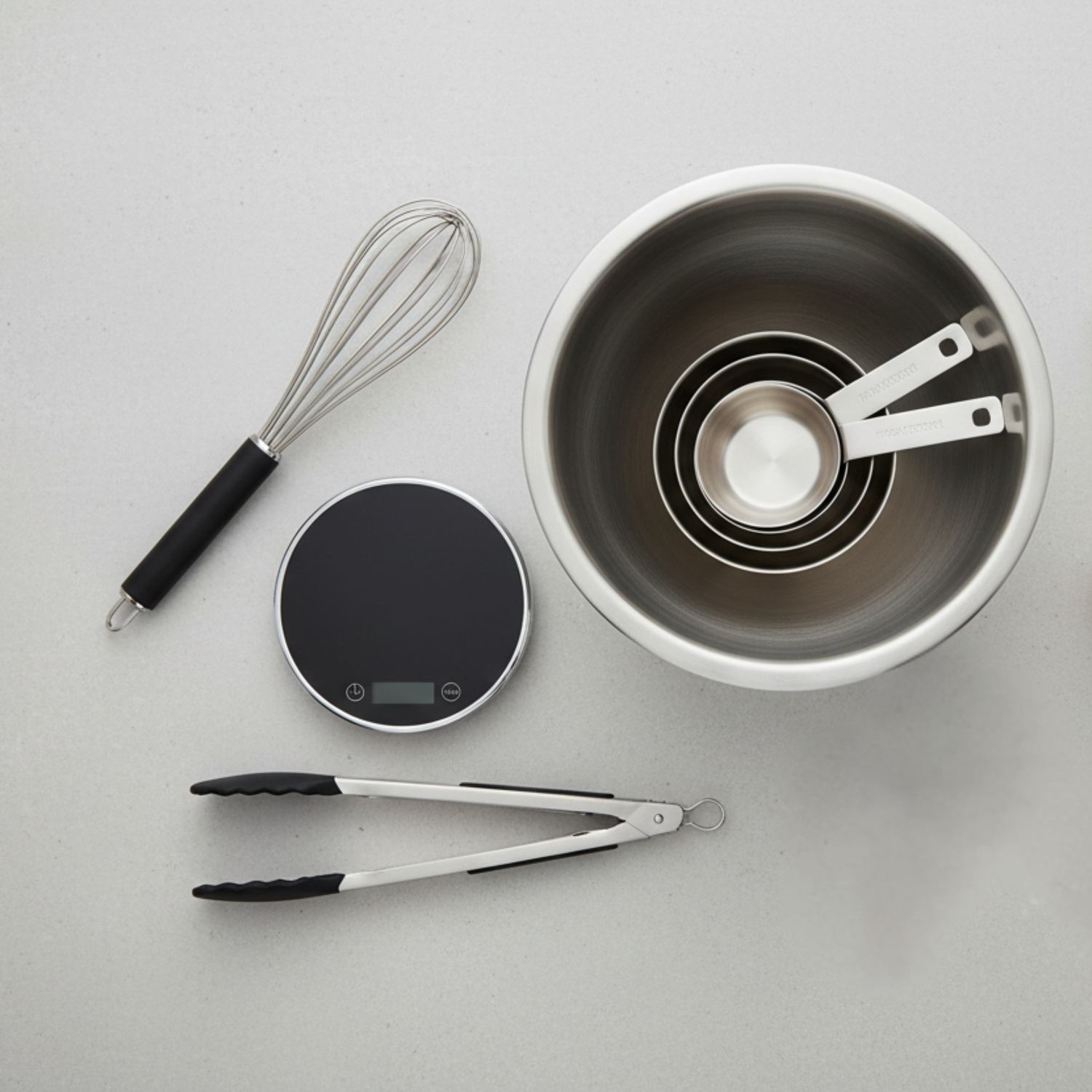 Kitchen accessories set including stainless steel mixing bowl, measuring cups, whisk, tongs, and digital kitchen scale on a light background